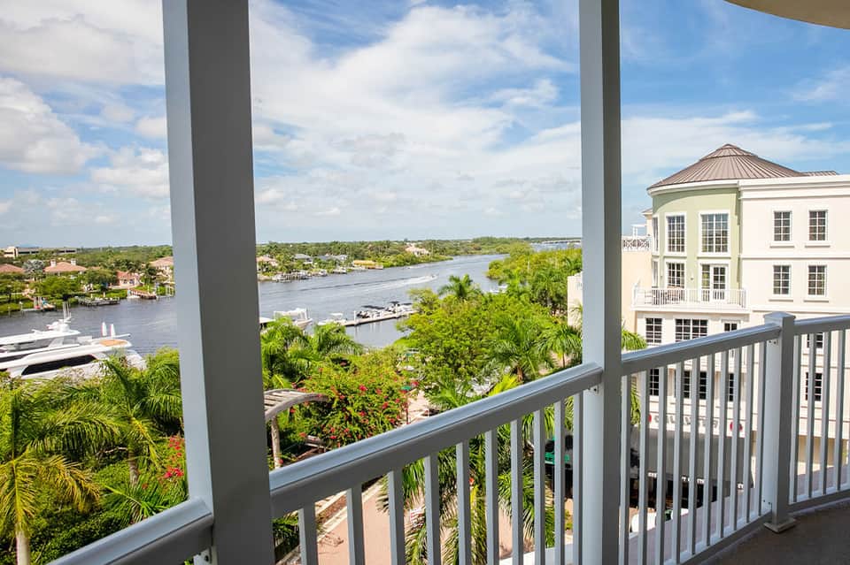 Waterfront balcony view overlooking marina, river, and palm trees with residential buildings