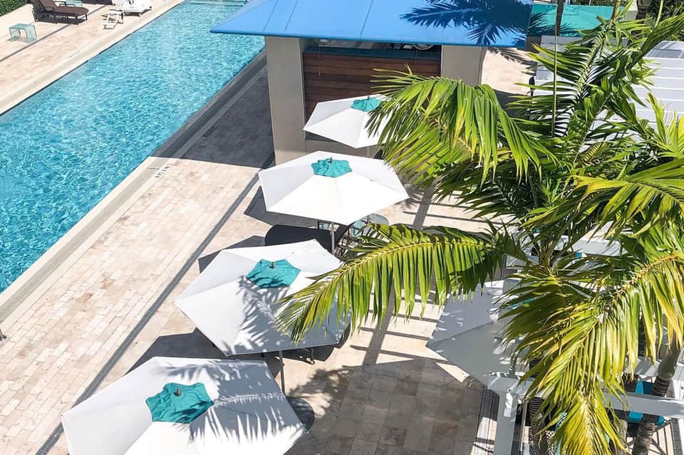 Aerial view of resort pools surrounded by white umbrellas and palm trees