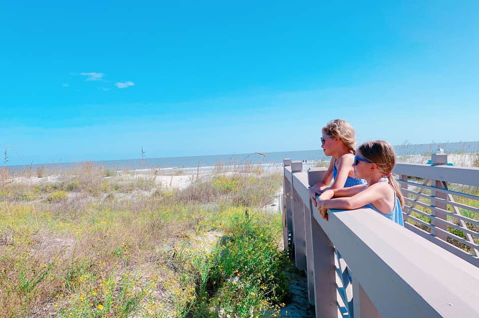 Two children on wooden beach boardwalk overlook dunes and ocean under clear blue sky