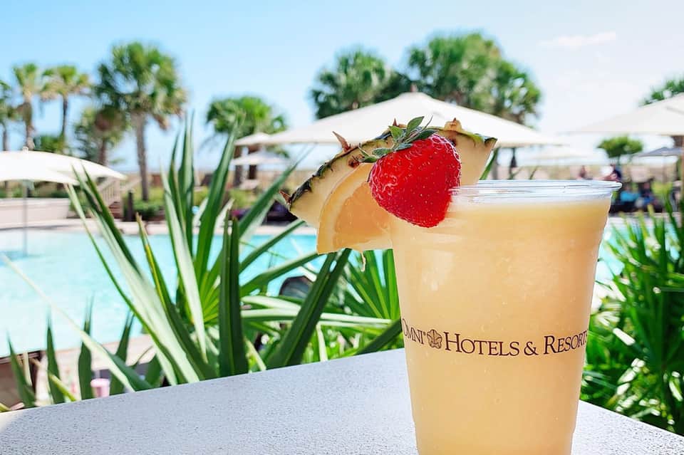 Poolside cocktail with strawberry garnish at beachfront resort with palm trees