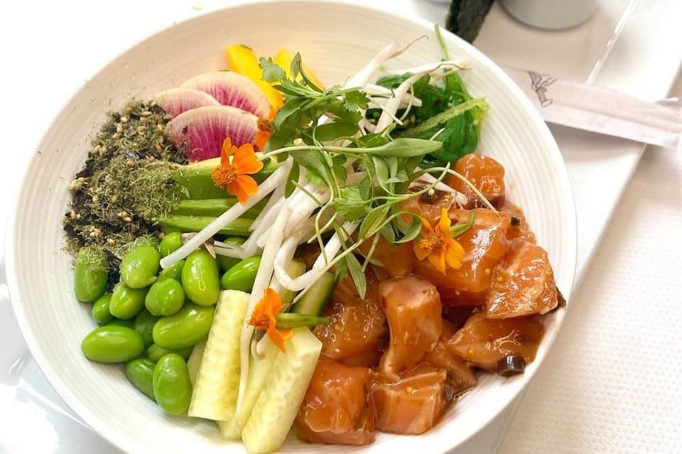 Colorful bowl with seared salmon, edamame, cucumber, seaweed salad, and edible flowers