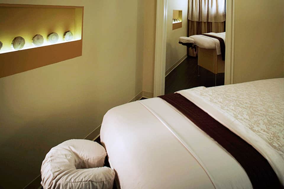 Modern hotel room with queen bed, illuminated wall niche with decorative items, and open doorway to adjacent space