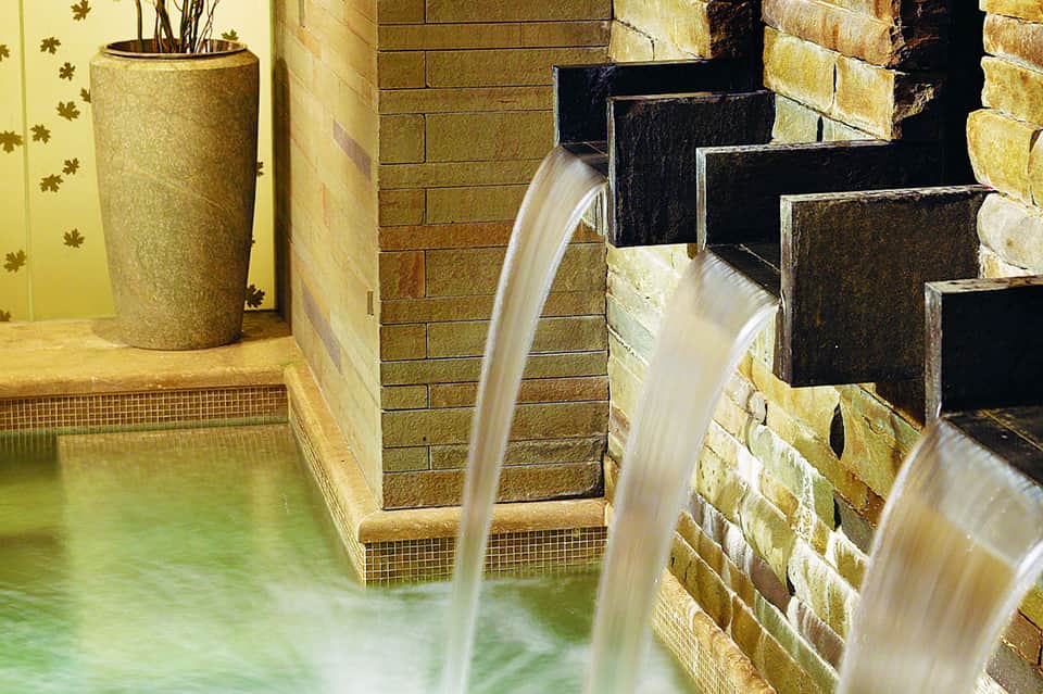 Spa waterfall features cascading water flowing into steaming mineral pool with brick walls