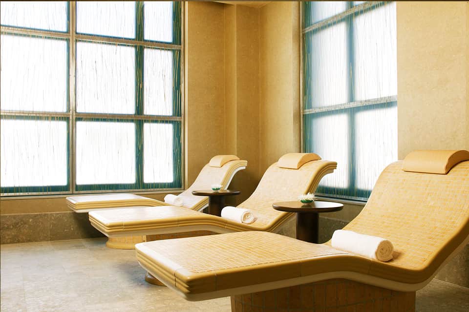 Luxury spa relaxation room with cream loungers, large windows with green trim, and minimalist décor