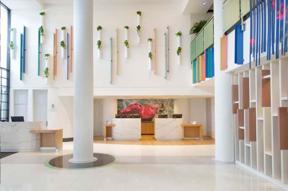 Modern hotel lobby with white marble reception desk, colorful wall plants, and hanging greenery