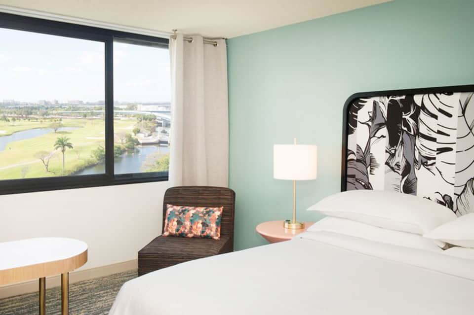 Modern hotel bedroom with mint green walls, white bedding, and large window overlooking scenic landscape