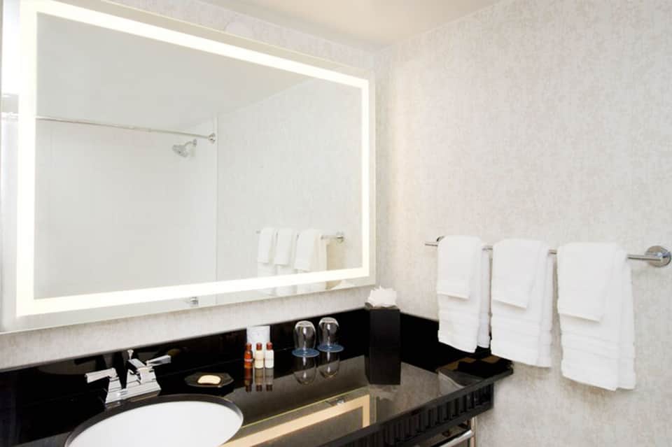 Luxury bathroom vanity with illuminated mirror, black countertop, and white towels