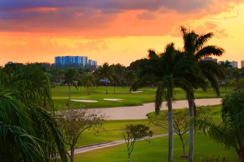 Golf course at sunset with palm trees, water features, and high-rise resort buildings in background