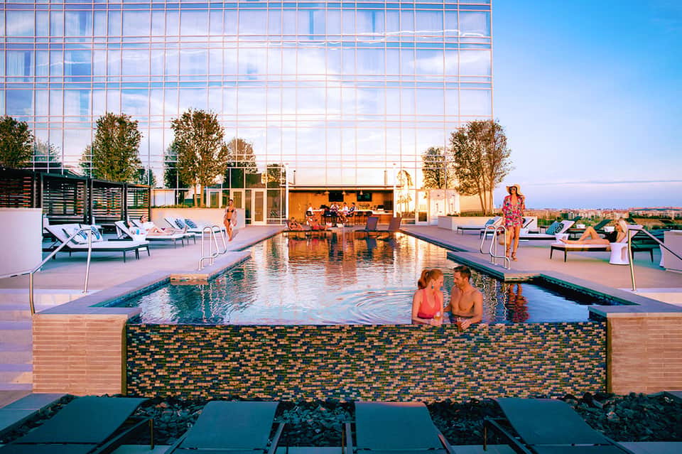 Rooftop pool with tiled wall feature, loungers, and modern glass building backdrop at sunset