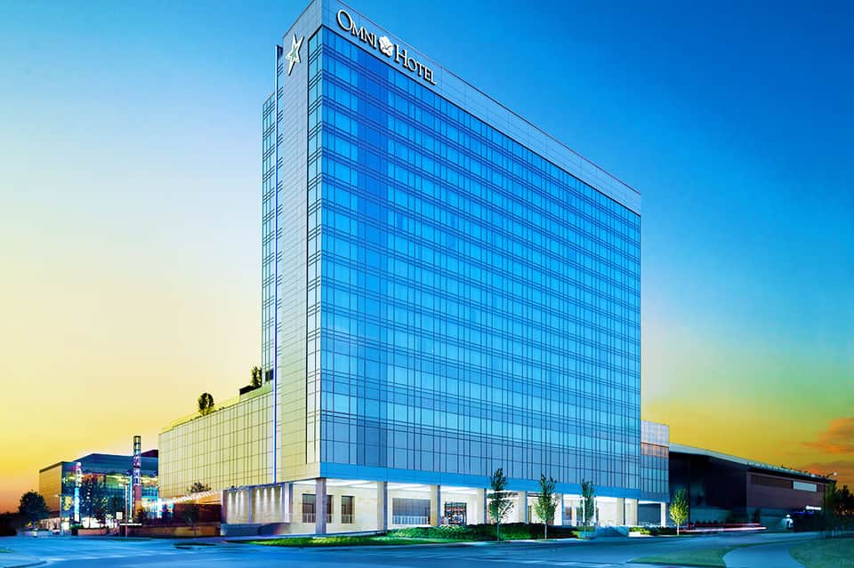 Modern Omni Hotel exterior at dusk with illuminated blue glass facade and white ground-level entrance