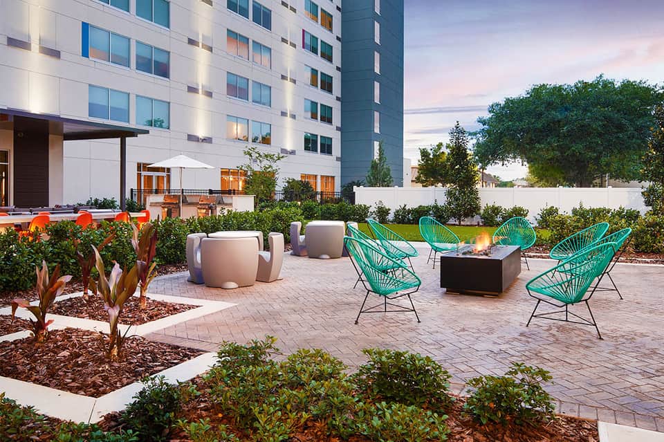 Modern courtyard with turquoise chairs, fire pit, and contemporary hotel building