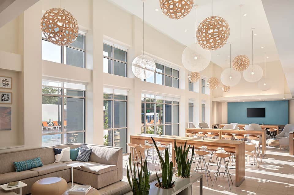 Modern hotel lobby with high ceilings, wooden pendant lights, lounge seating, and bright natural light