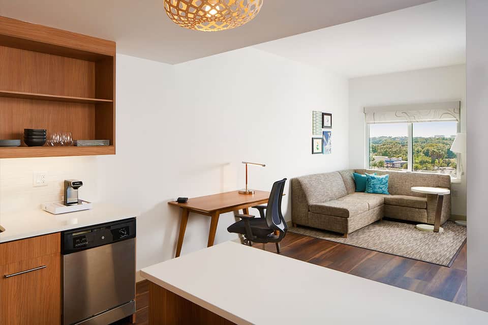 Modern studio apartment with kitchenette, work desk, and seating area overlooking green landscape
