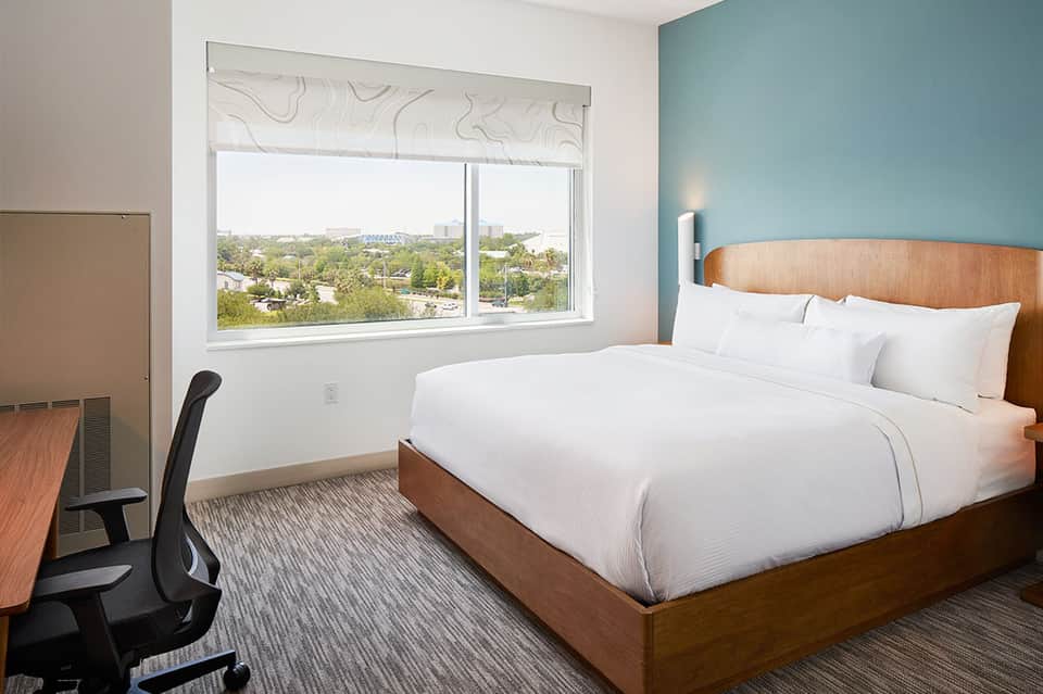 Contemporary bedroom with queen bed, turquoise accent wall, work desk, and large window with city views