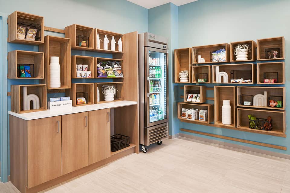 Contemporary wooden shelving system displaying beverages, décor items, and amenities in hotel café space
