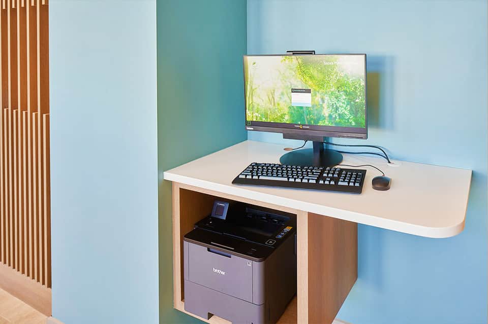 Modern workspace with desktop computer, keyboard, mouse, and printer on light wood desk against blue wall