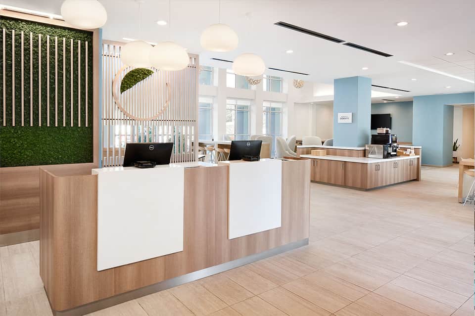 Hotel lobby with wood reception desk, pendant lighting, green plant wall, and modern décor
