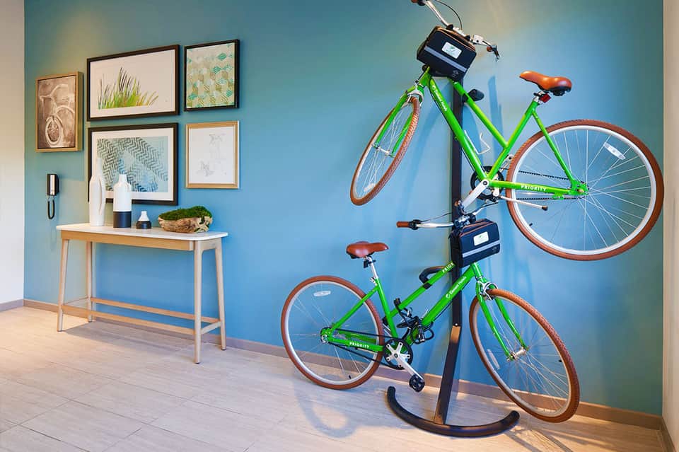 Modern hotel entry with bright blue wall, two green bikes on display stand, wooden console table with decor, and framed botanical artwork