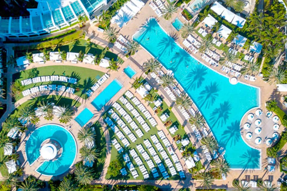 Aerial view of resort with multiple turquoise pools, palm trees, and lounge chairs arranged throughout the grounds