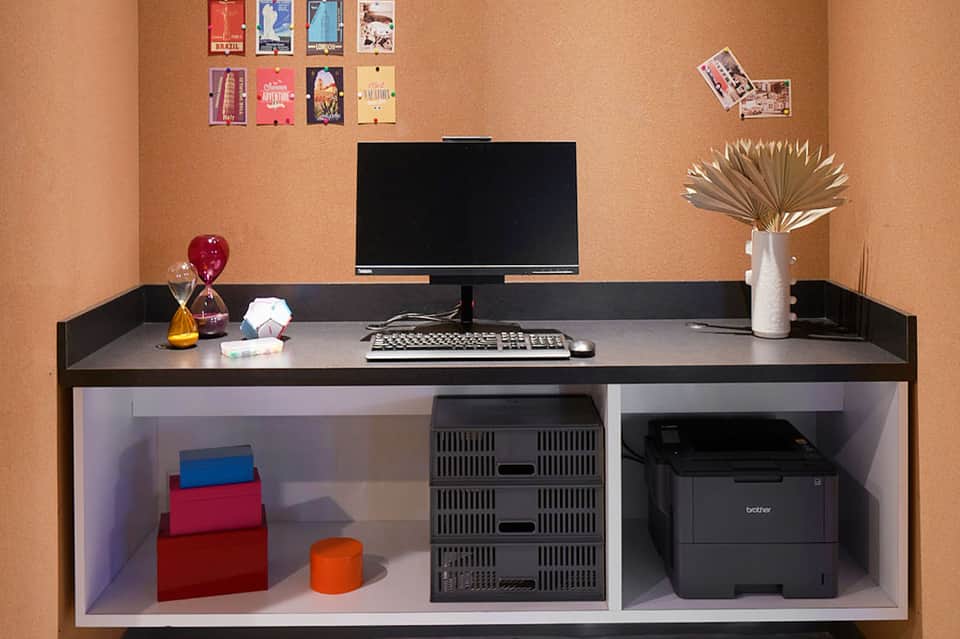 Home office desk with black monitor, keyboard, decorative items, and storage shelving with organized supplies
