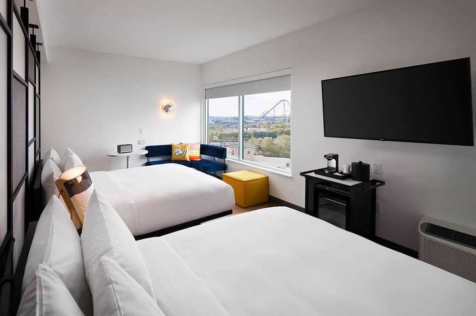 Modern hotel room with two beds, ocean view, blue accent chairs, and flat-screen TV