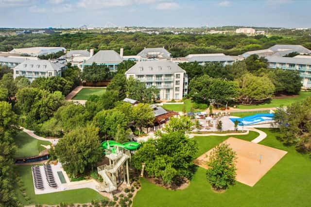 Aerial view of luxury resort with swimming pool, sports courts, and manicured grounds surrounded by trees