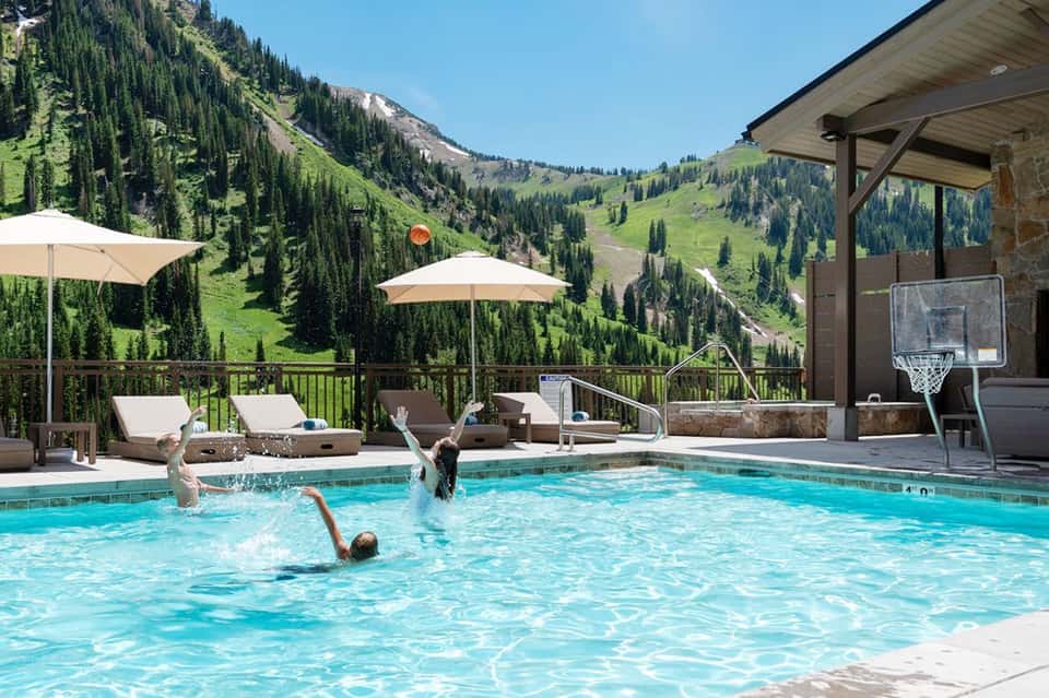 Mountain resort pool with guests swimming, overlooking scenic alpine valley landscape