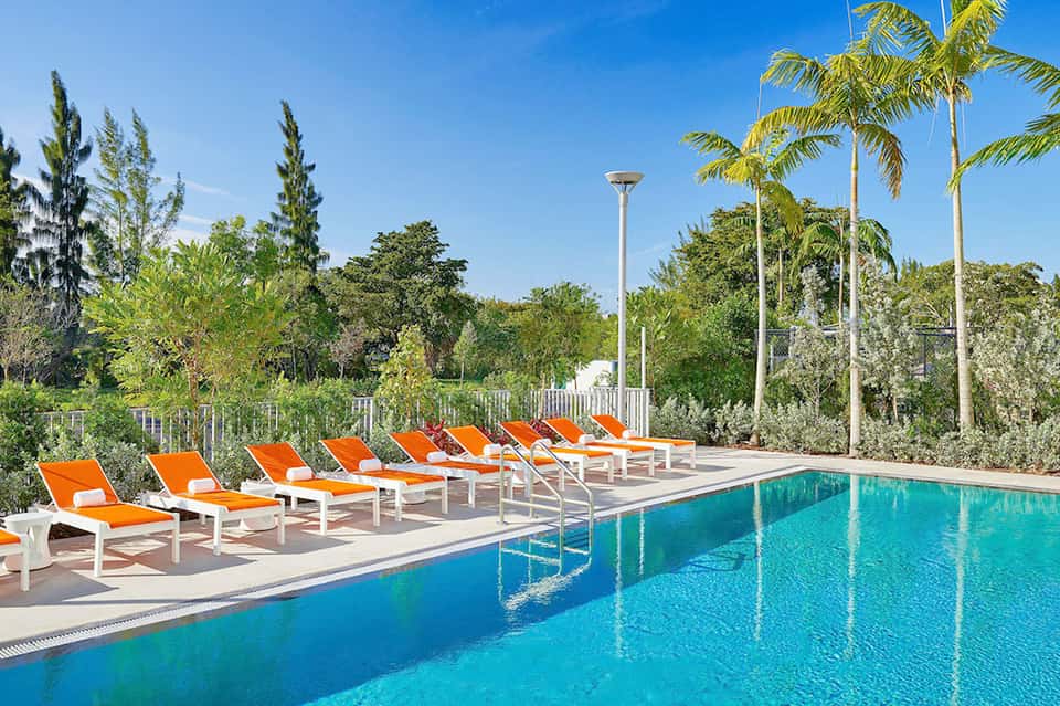Resort swimming pool with bright orange lounge chairs and tropical palm trees under blue sky