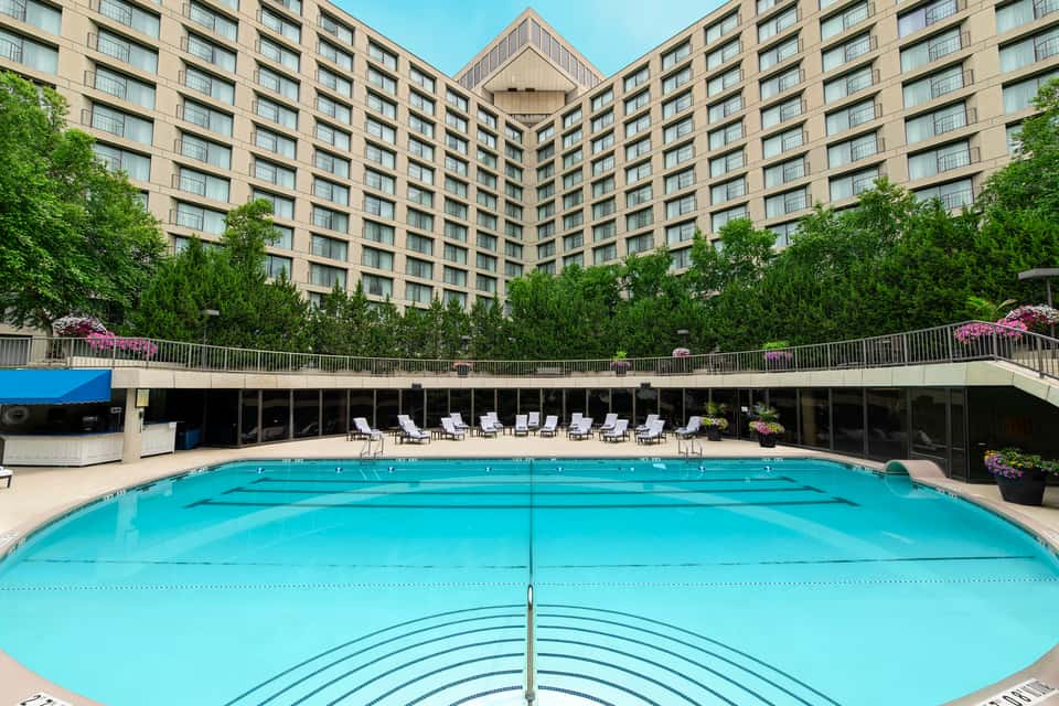 Large rectangular swimming pool with lane markings, surrounded by lounge chairs and tall hotel building