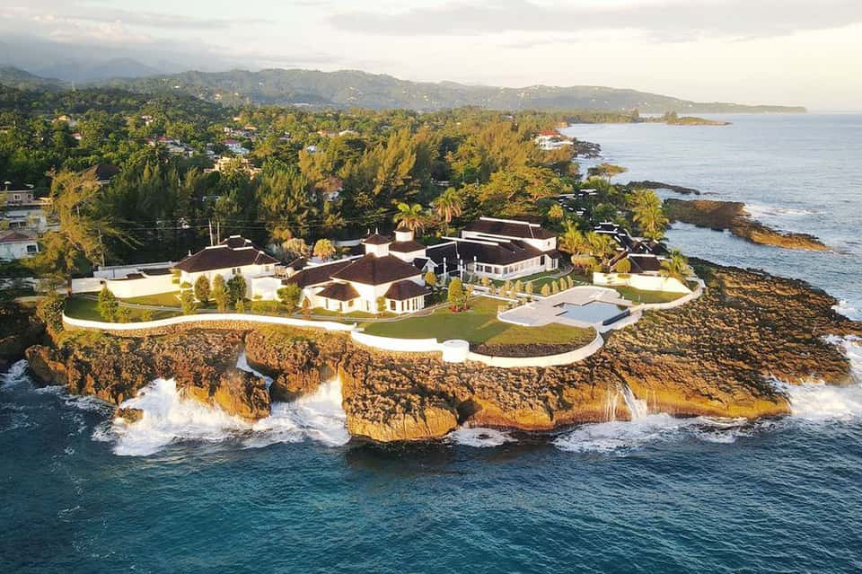 Luxury clifftop residence with white architecture on rocky coastline surrounded by tropical vegetation