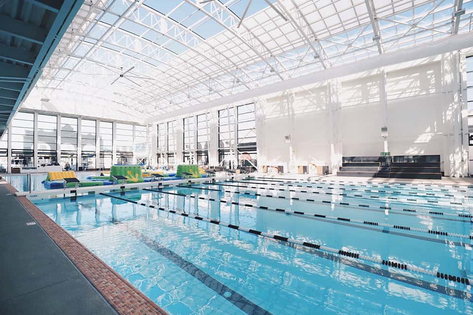 Bright indoor Olympic-size swimming pool with lap lanes under expansive glass ceiling and skylights
