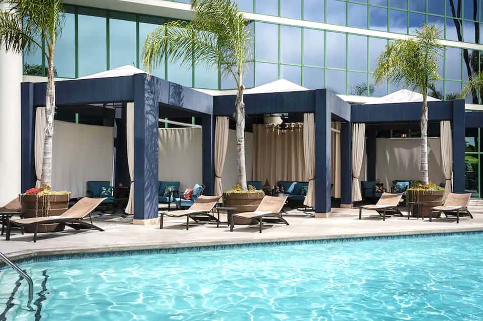 Resort pool with black cabanas, white curtains, and palm trees during daytime