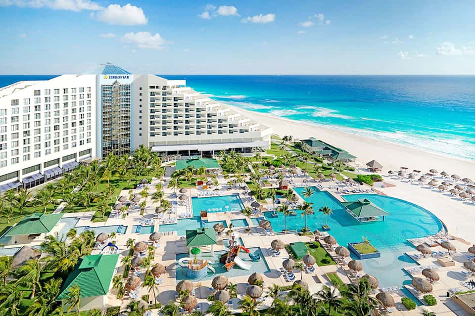 Beachfront resort with white buildings, turquoise pools, sandy beach, and pristine ocean waters