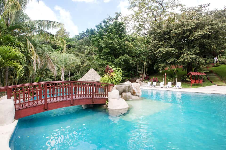 Resort pool with red bridge, tropical landscaping, and lounge chairs in a natural garden setting