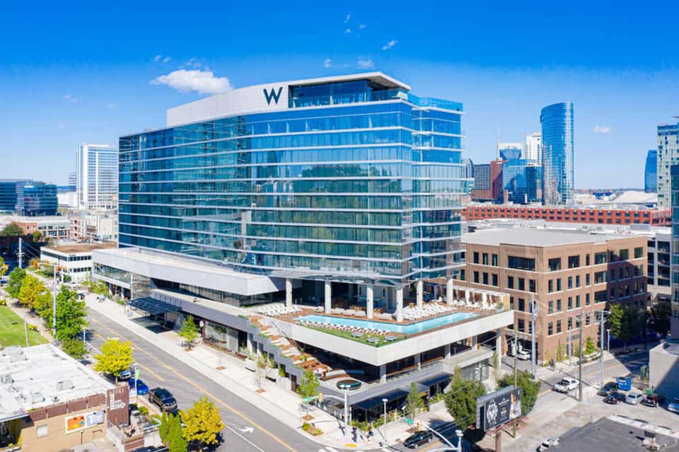 Modern blue and white hotel building with rooftop pool and lounge area in downtown urban setting.