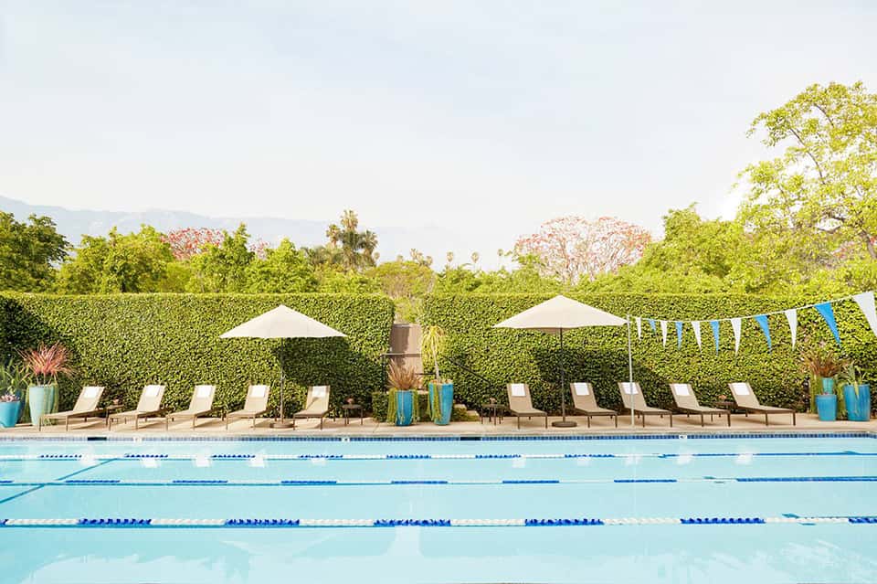 Lap pool with lane dividers, lounge chairs, and umbrella shade beneath trees and mountains