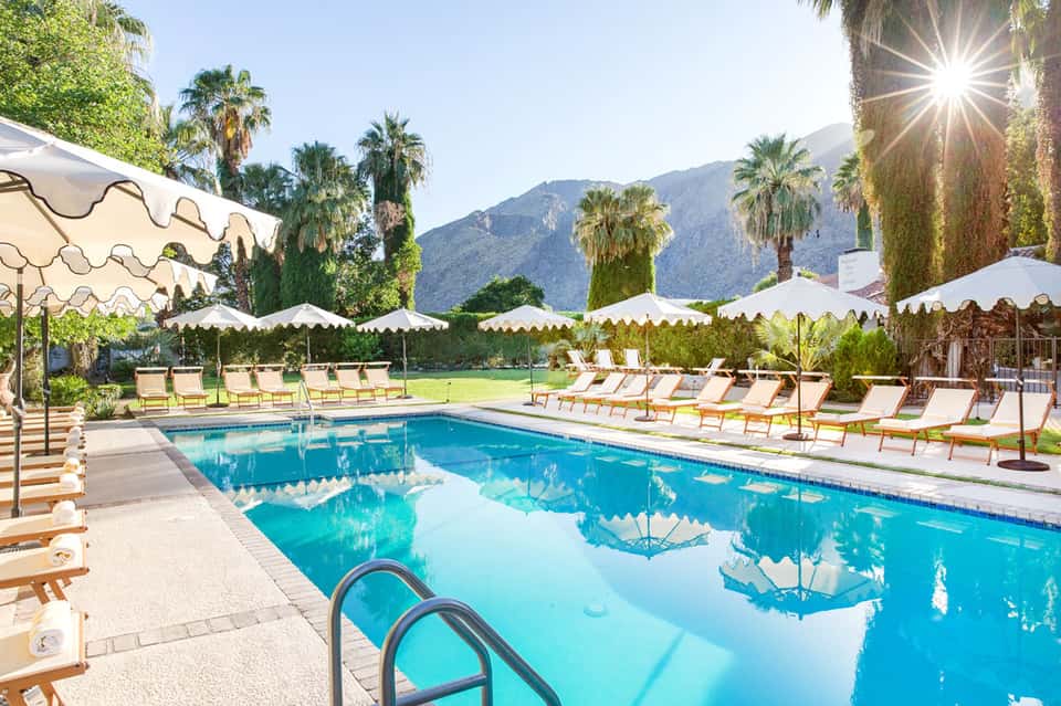 Resort pool with cream umbrellas, palm trees, and mountain backdrop