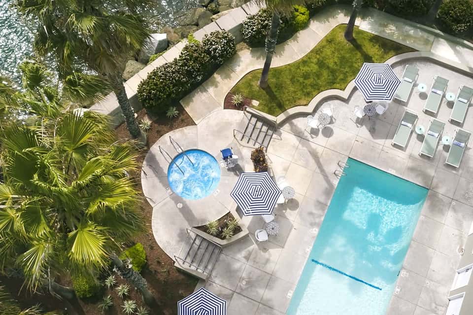 Aerial view of resort pool and spa area with palm trees, loungers, and manicured grounds