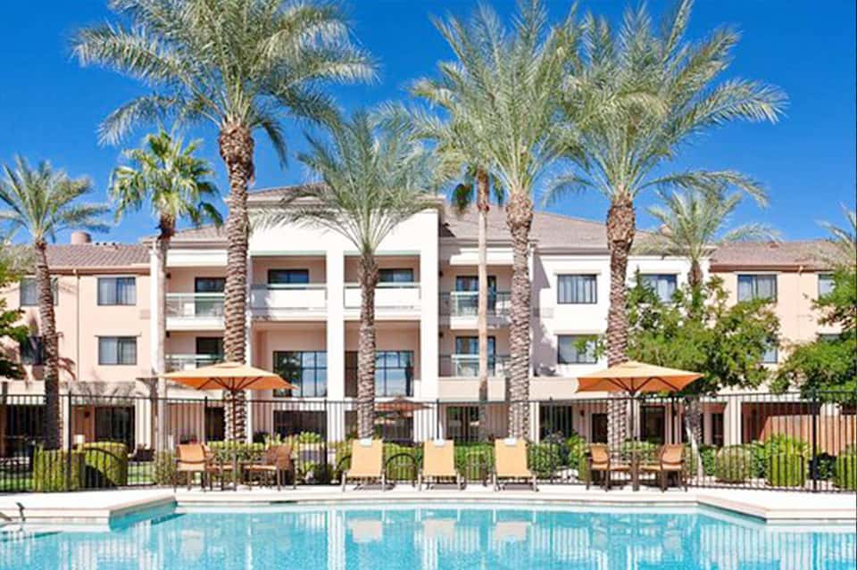 Resort building with palm trees, lounge chairs, umbrellas, and pool in foreground