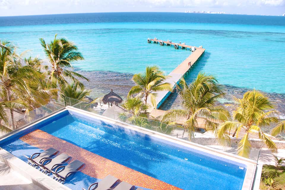 Oceanfront resort pool with turquoise water, palm trees, pier, and tropical beach view