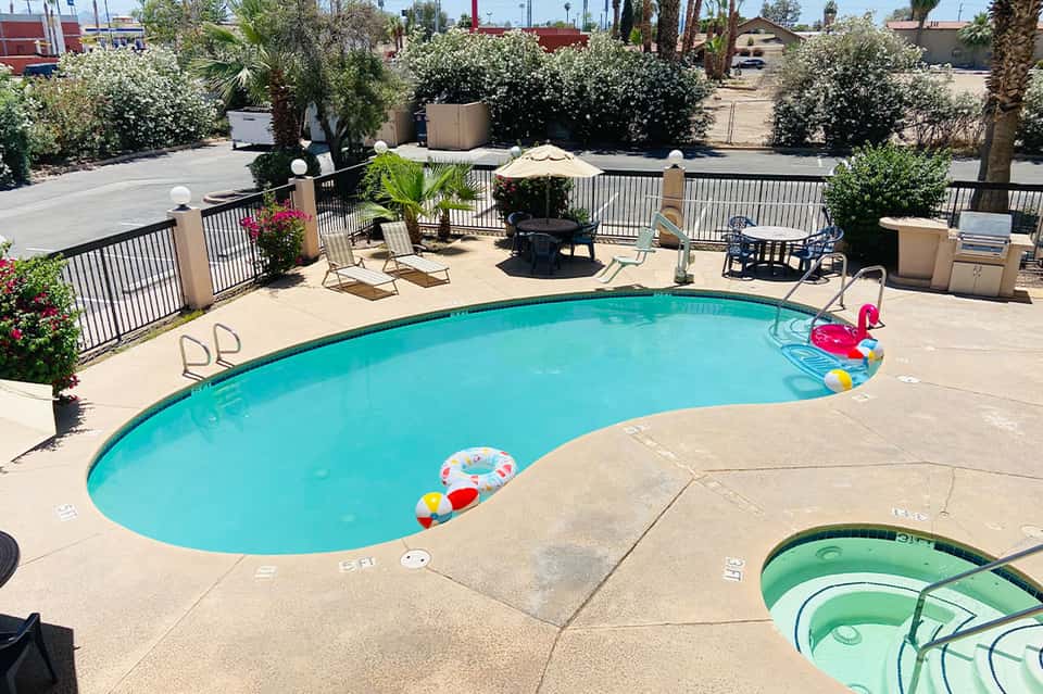 Resort pool with turquoise water, lounge chairs, fire pit, and palm trees under sunny desert sky