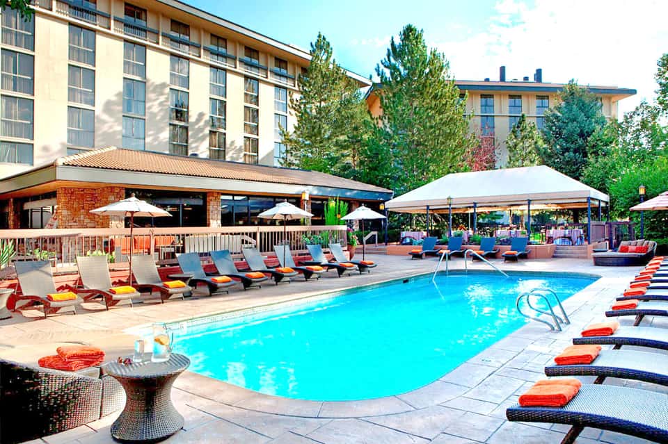 Resort swimming pool surrounded by lounge chairs, umbrellas, and multi-story hotel building