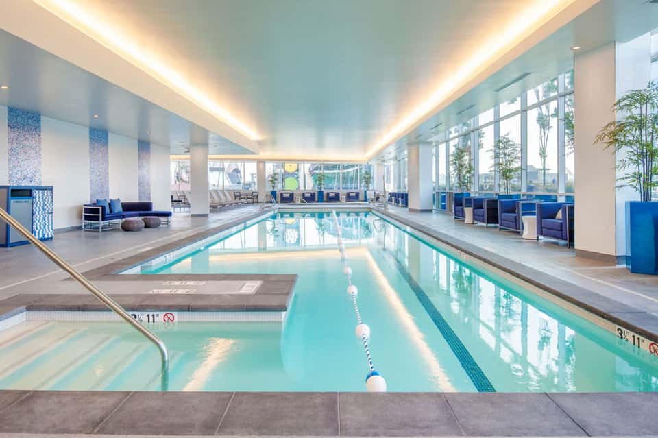 Indoor lap pool with lane dividers, modern lighting, blue accents, and floor-to-ceiling windows