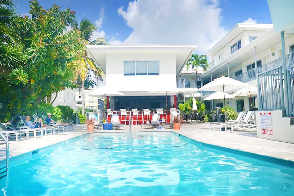 Resort pool with tropical landscaping, white umbrellas, and palm tree-lined courtyard