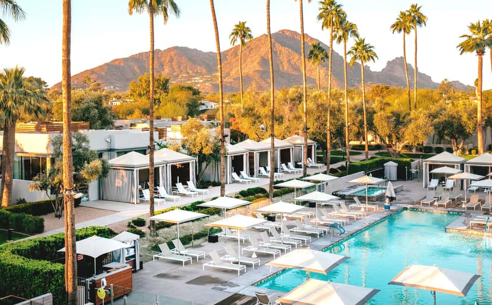 Luxury resort pool with lounge chairs, white cabanas, and palm trees against desert mountain backdrop