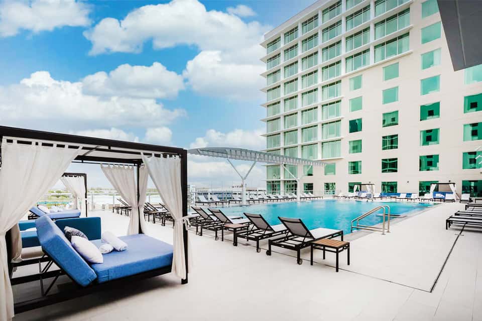 Resort pool area with cabanas, lounge chairs, and multi-story hotel building