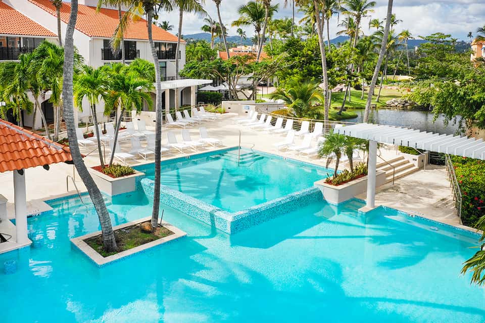 Resort pool with turquoise water, white loungers, palm trees, and tropical landscaping