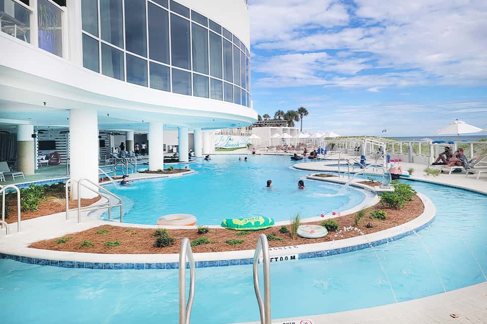 Resort pool complex with lazy river, multiple pools, and palm trees under blue sky