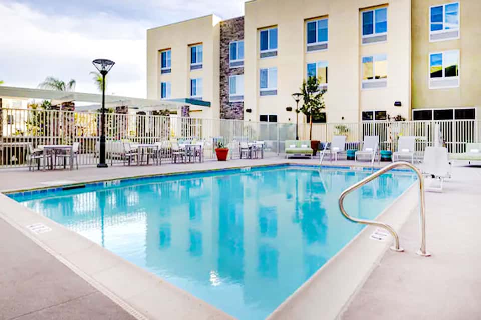 Modern hotel pool with white railings and multi-story beige building
