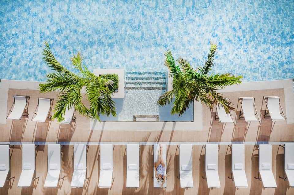Aerial view of resort pool with sunbathing guests and palm trees